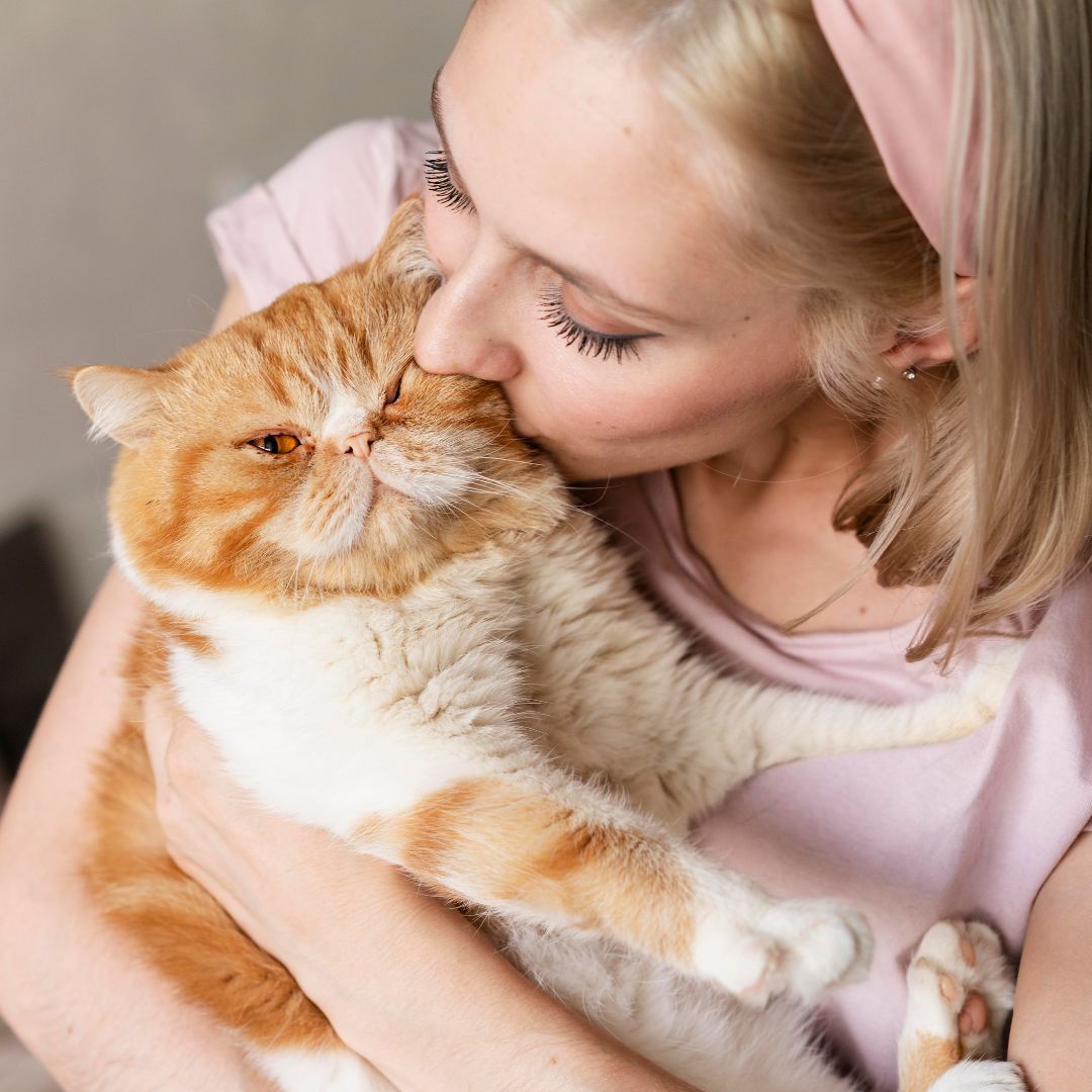 Woman kissing an orange and white cat on a neutral background